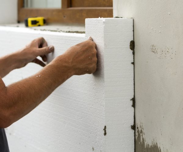 Worker hands installing white rigid polyurethane foam sheet on plastered brick wall. Modern technology, renovation, insulation concept.